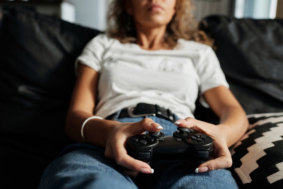A woman relaxing on a sofa playing video games at home, focusing on a controller.