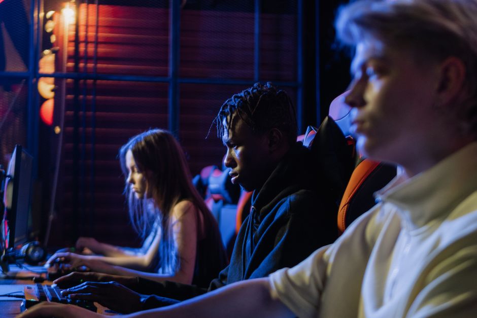 Three young gamers intensely focused on their video gaming session in a dimly lit room, using computers.