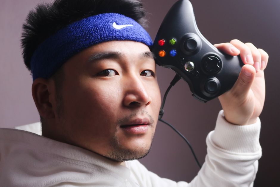 Asian man in white sweatshirt holding a gaming controller, focused on gaming.