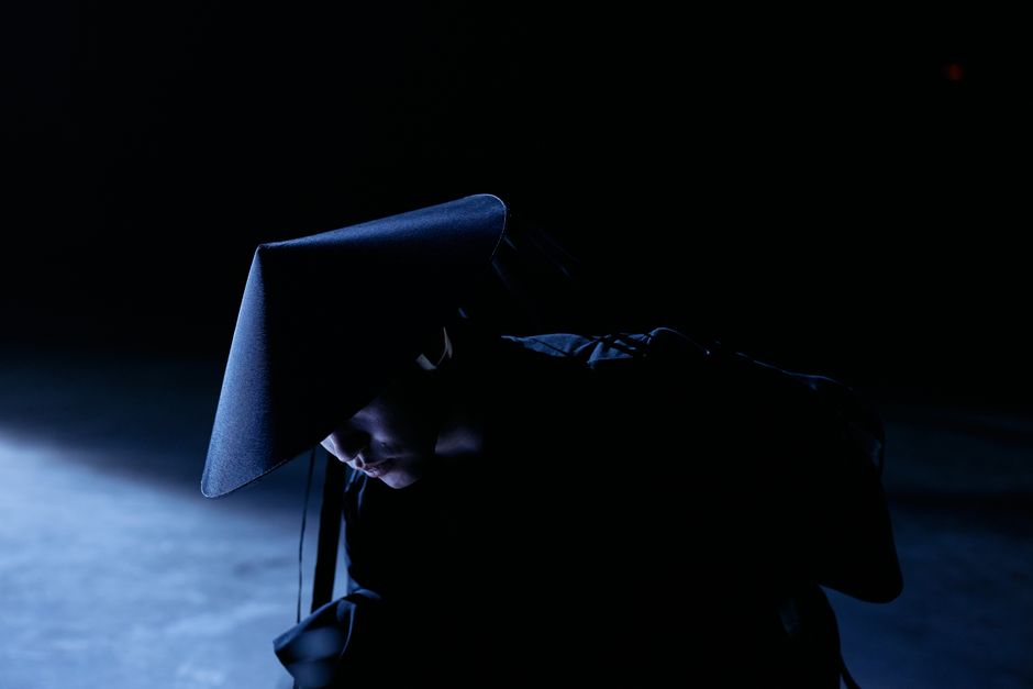 A mysterious figure in cosplay costume with a sakkat in a dark studio setting, conveying intrigue and concept.
