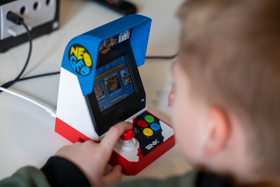 A child engaging with a Neo Geo mini arcade machine, enjoying retro gaming indoors.