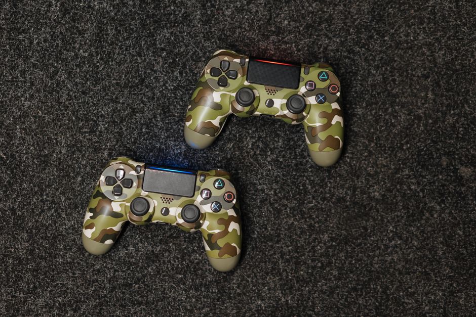 Close-up view of two camouflage-patterned gaming controllers on a textured surface.