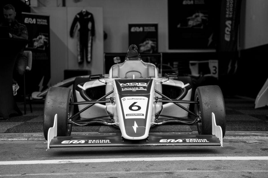 Black and white photo of a Formula racing car inside a garage, showcasing the vehicle's front.