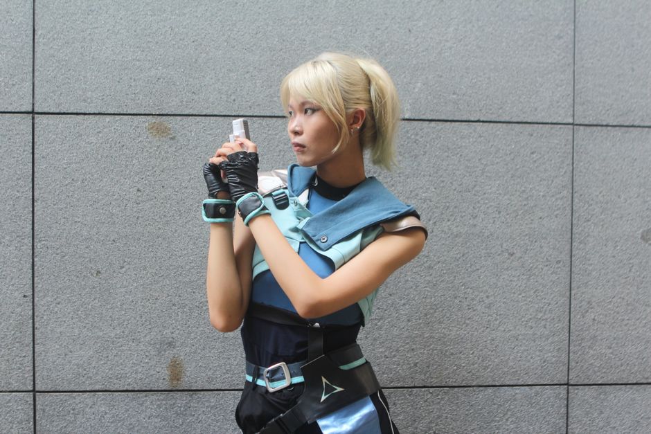 Young woman in futuristic cosplay outfit holding a blaster, posing against a neutral background.