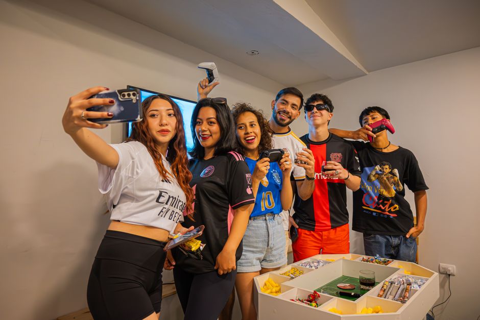 A cheerful group of friends having fun indoors, playing video games and taking selfies.