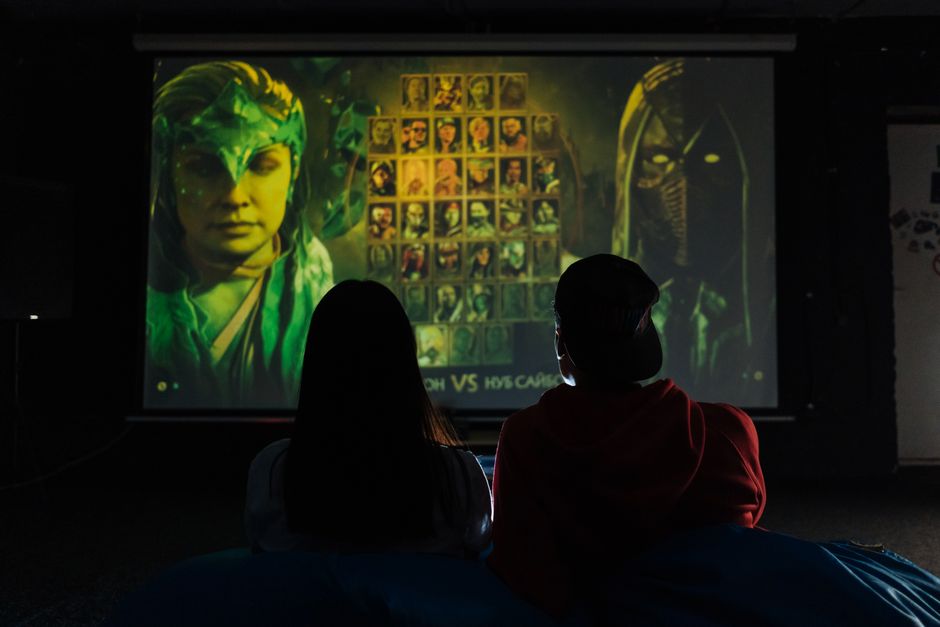 Two people sitting indoors gaming on a large projector screen, enjoying a video game session.