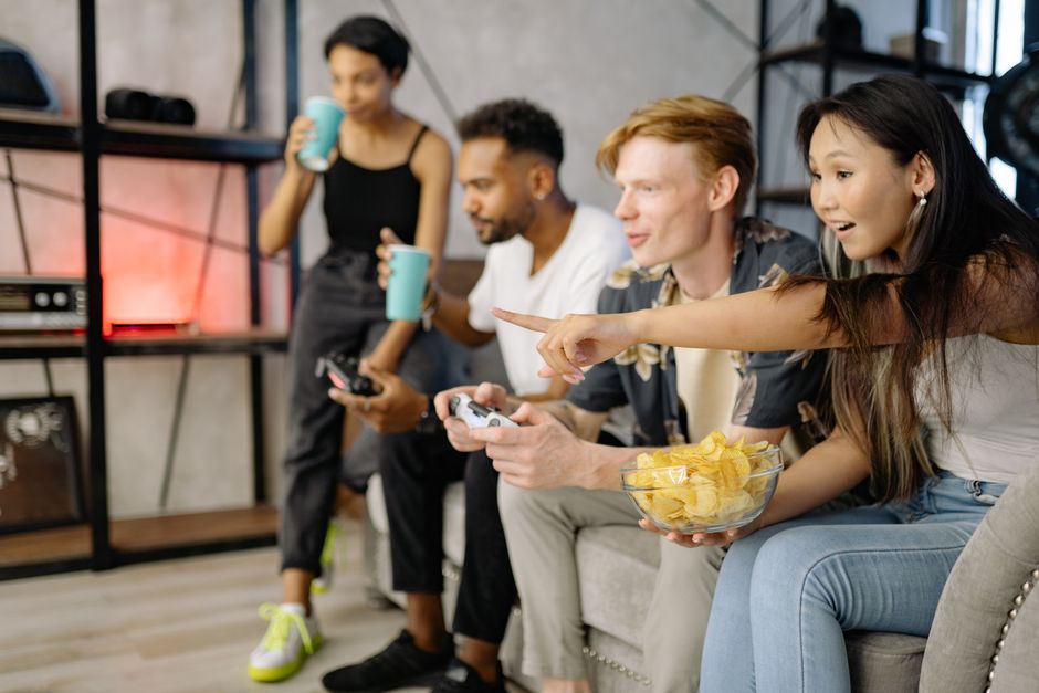 Diverse group of friends enjoying video games and snacks in a cozy living room setting.